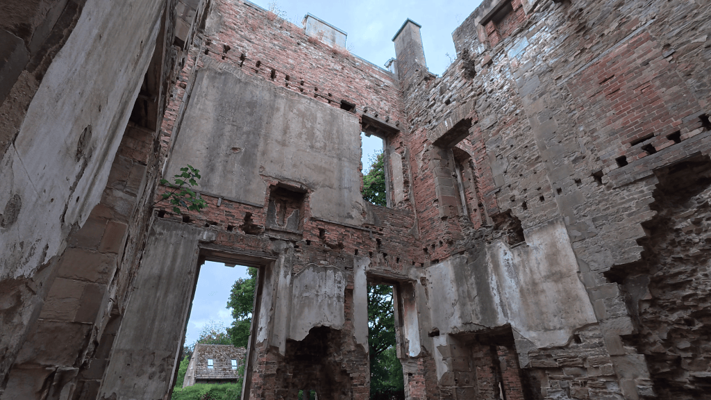 Interior view of a partially collapsed brick building, showing crumbling walls and openings to the sky.